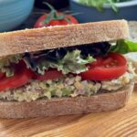 chickpea sandwich spread in a sandwich with tomatoes and lettuce served on a board