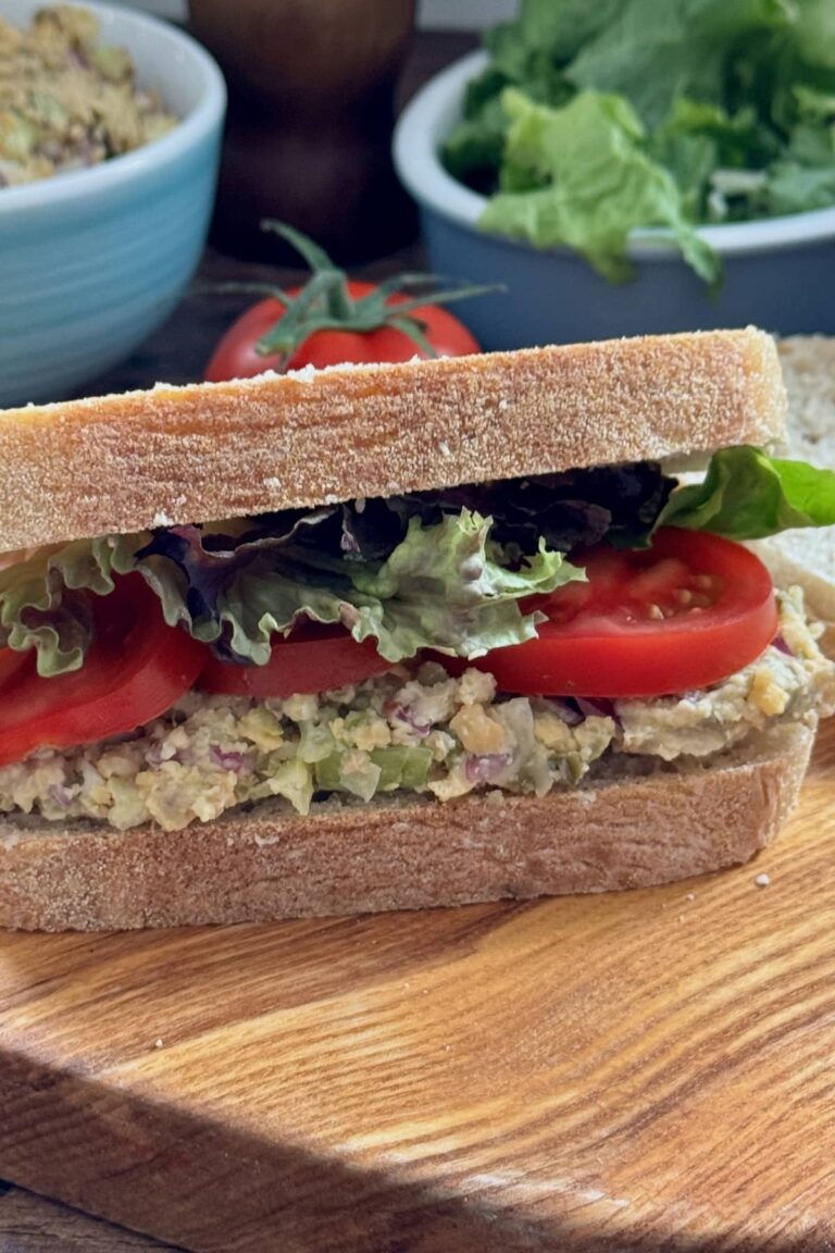 chickpea sandwich spread in a sandwich with tomatoes and lettuce served on a board