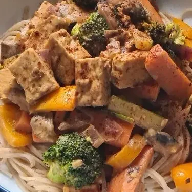 A tempeh stir fry with peanut and lime sauce served with noodles