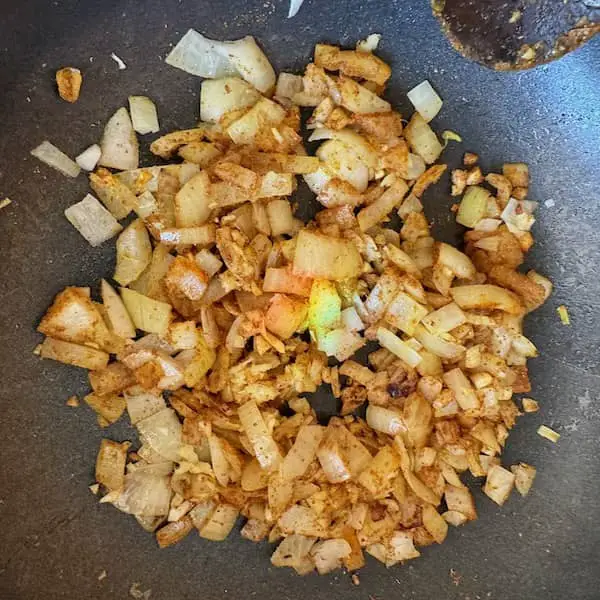 onions mixed with spices cooking in a pan as a base for a black bean curry