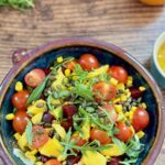 mango and beet salad served in a salad bowl with oranges and dressing in the background