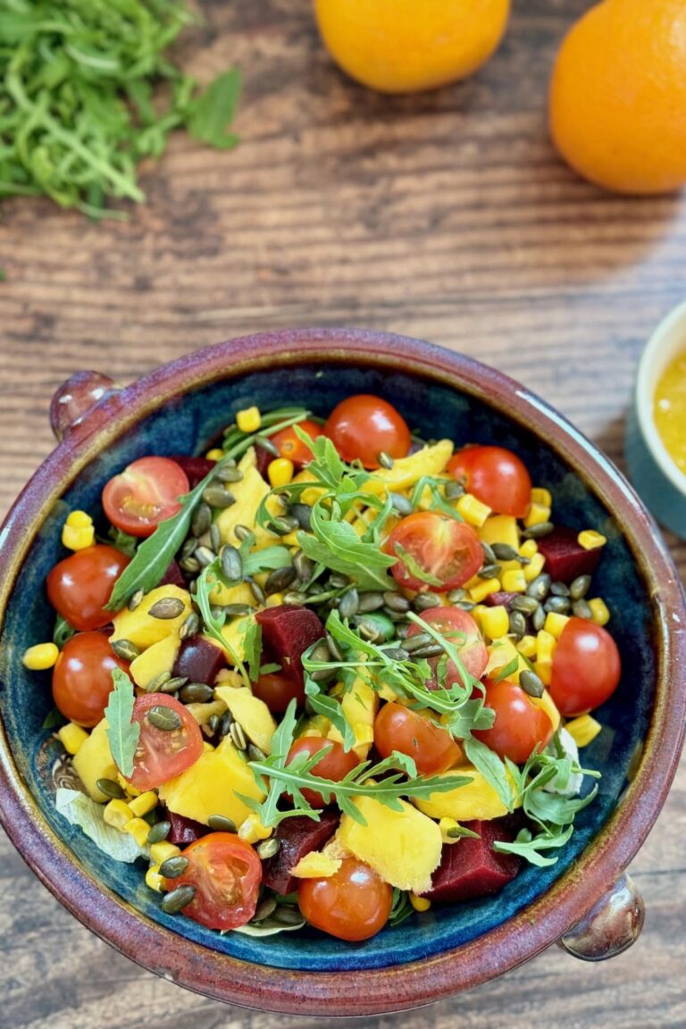 mango and beet salad served in a salad bowl with oranges and dressing in the background