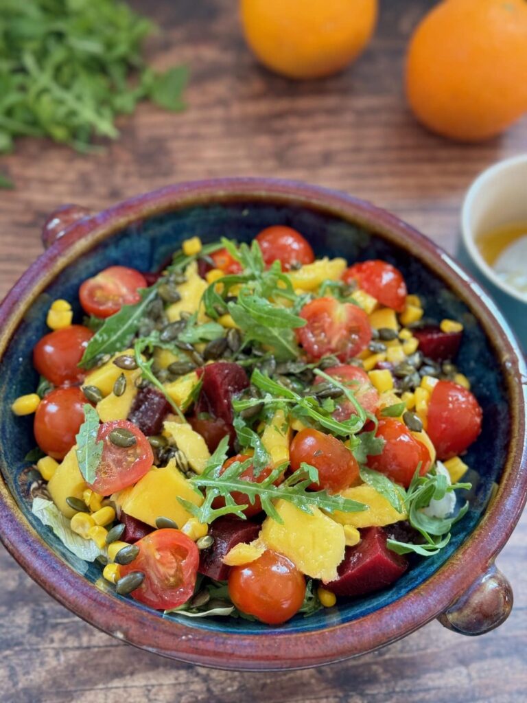 mango and beet salad served in a salad bowl with oranges and dressing in the background