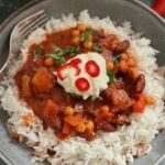 veggie and bean chilli served with rice on a plate and topped with soy yoghurt