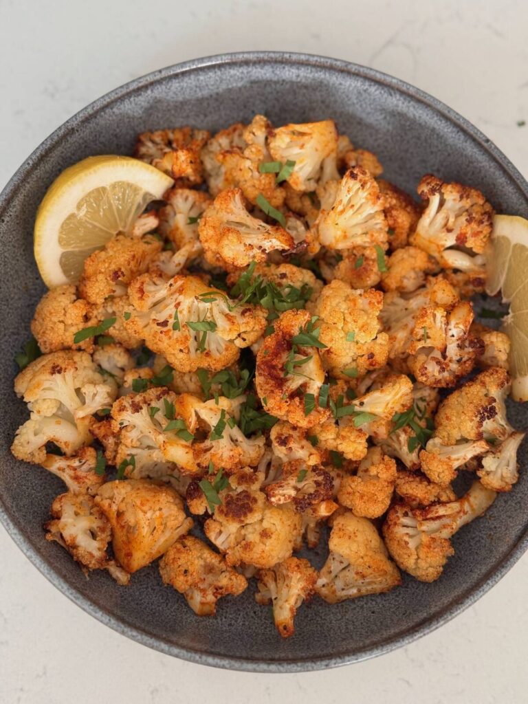 roasted cauliflower with spices presented in a bowl with lemon wedge and parsley